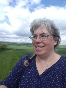 Photo of Jo Nash the Creator in the coutryside with green fields and blue sky.