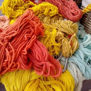 pile of naturally dyed yarns, including red, orange, yellow and pale blue
