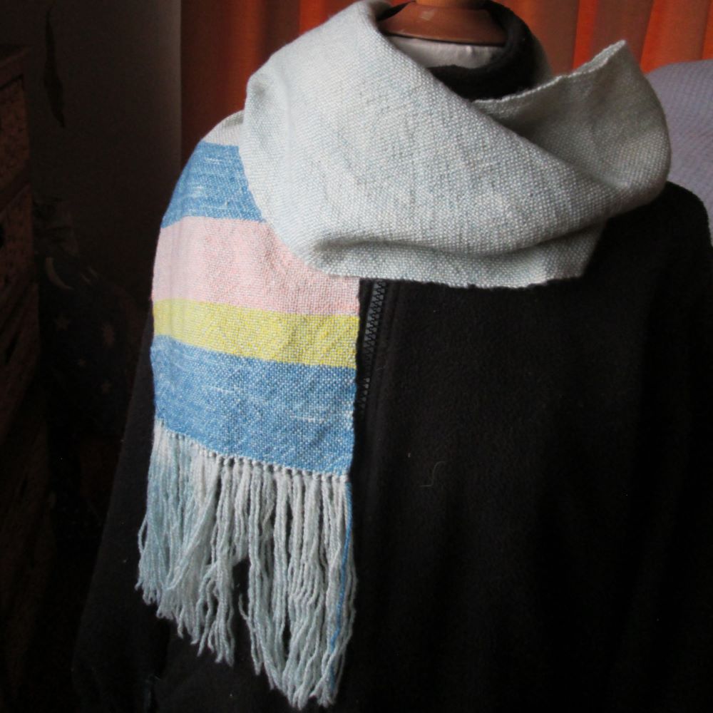 scarf wrapped around a mannequin with a black jacket. The end of the scarf is dark blue, yellow and pink stripes