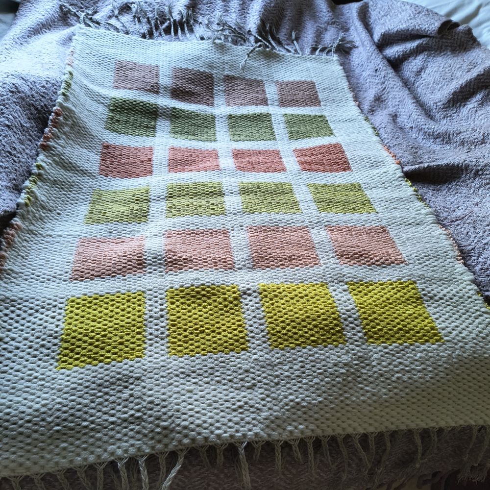 rug with a white background and coloured squares ranging from bright yellow through pink, green and red to brown at the back