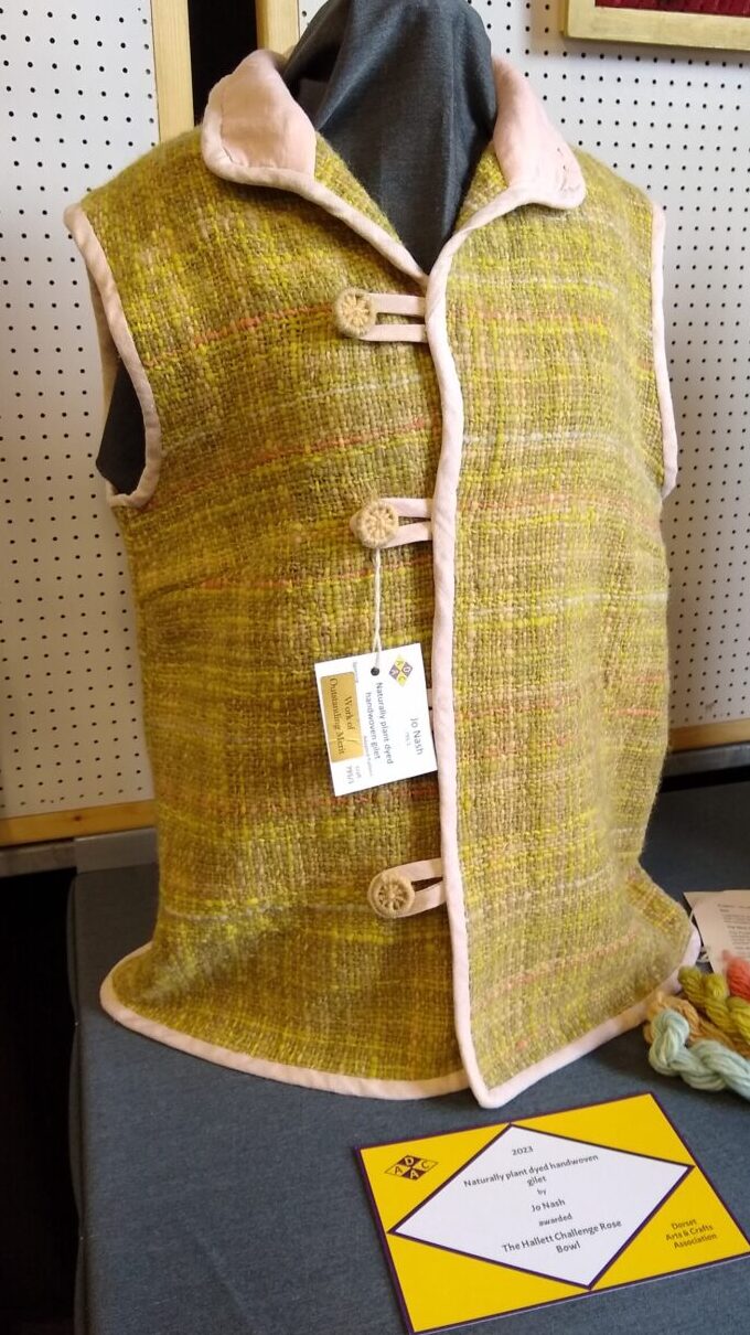 Olive green gilet on a mannikin with a gold prize card in front and a cream background