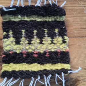 Coaster with a Christmas tree design on a black background laying on a wooden table top