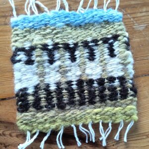 Five sheep on a green background with blue at the top of the design on a wood background